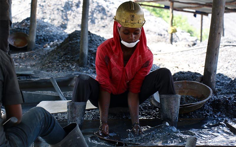 Female artisanal and small-scale miner panning for minerals wearing safety equipment.
